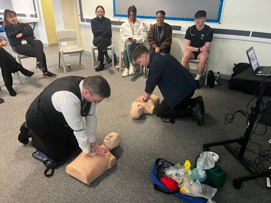 First aid trainer demonstrating CPR on a manikin to a group of seated delegates
