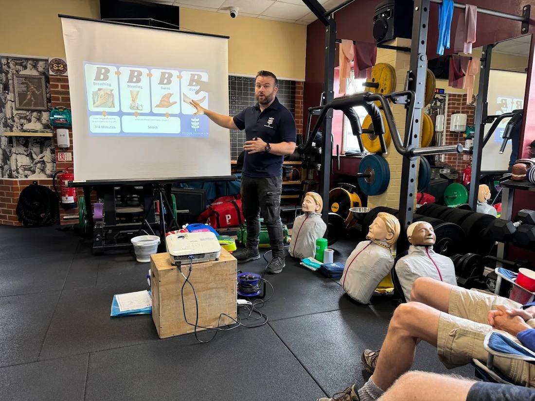 First aid trainer delivering a session with a presentation, with practice manikins ready for delegates